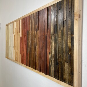 May include: A rectangular wooden wall art piece with a natural wood frame. The wood is arranged in a vertical pattern with different shades of brown, red, and white.