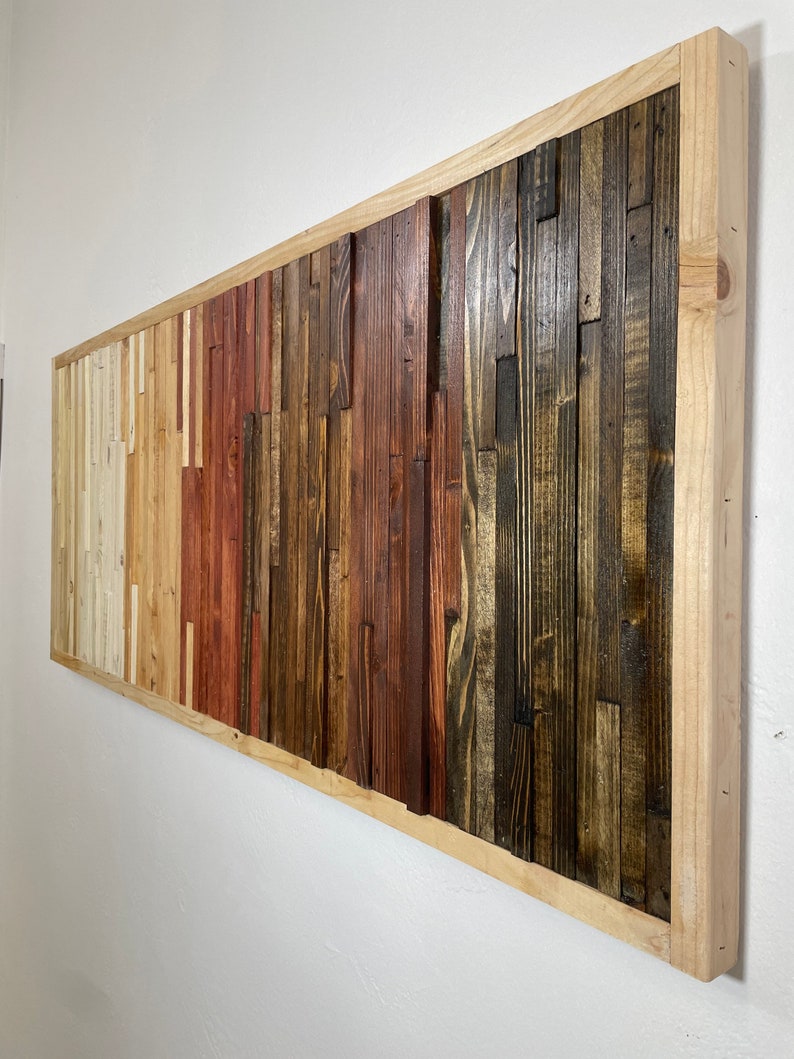 May include: A rectangular wooden wall art piece with a natural wood frame. The wood is arranged in a vertical pattern with different shades of brown, red, and white.