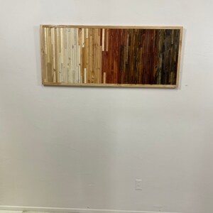 May include: A rectangular wooden wall art piece with a frame. The wood is arranged in horizontal strips, with the colors transitioning from white to brown.