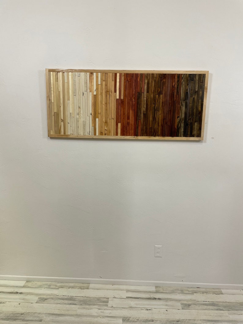 May include: A rectangular wooden wall art piece with a frame. The wood is arranged in horizontal strips, with the colors transitioning from white to brown.