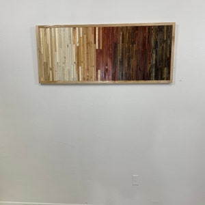 May include: A rectangular wooden wall art piece with a gradient of colors from light to dark. The piece is made of many small wooden slats arranged in vertical rows. The colors range from white to light brown to dark brown to red.