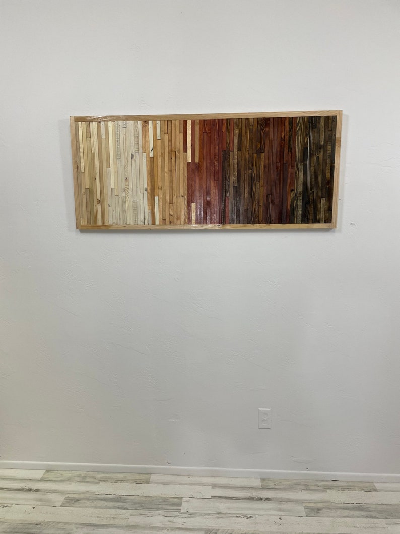 May include: A rectangular wooden wall art piece with a gradient of colors from light to dark. The piece is made of many small wooden slats arranged in vertical rows. The colors range from white to light brown to dark brown to red.