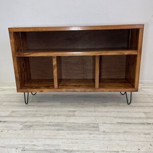 May include: A wooden shelf unit with four compartments and a top shelf. The shelf unit has black hairpin legs and a dark brown stain.