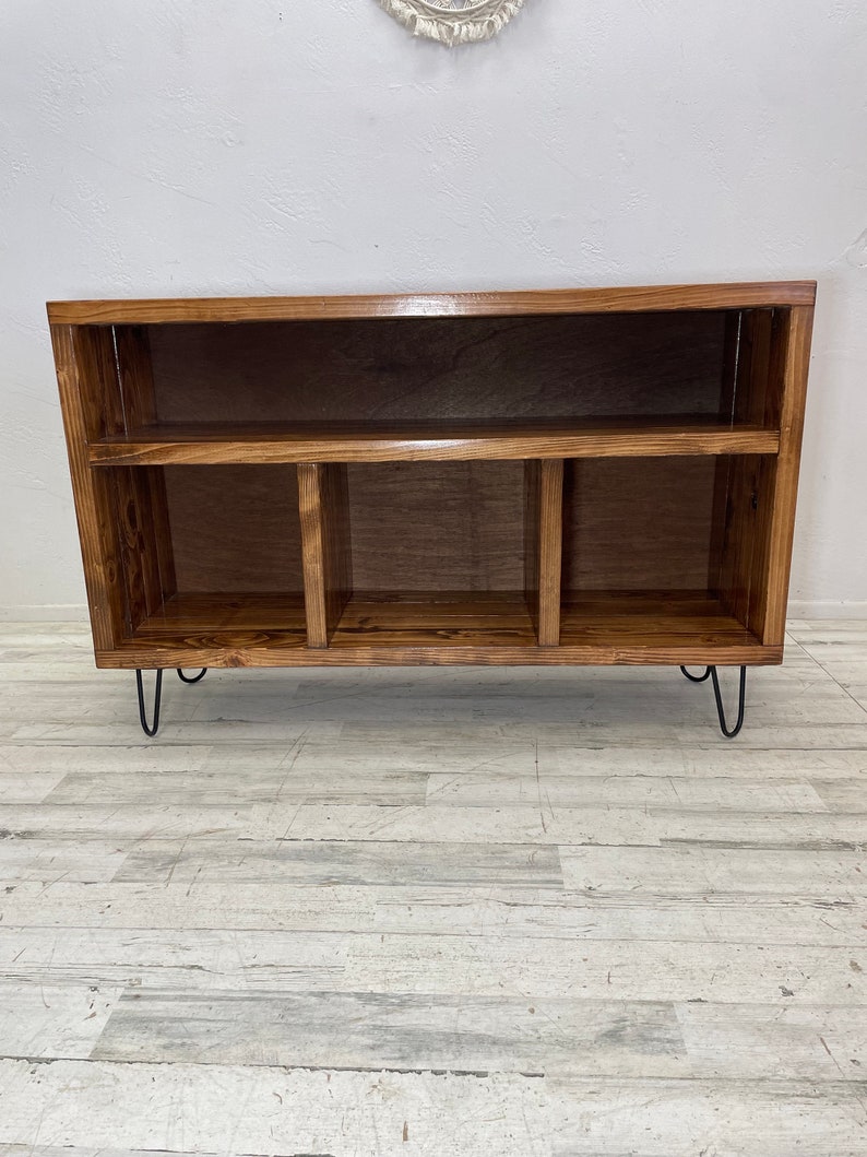 May include: A wooden shelf unit with four compartments and a top shelf. The shelf unit has black hairpin legs and a dark brown stain.