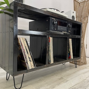 May include: Black wooden record player stand with four shelves, a turntable, and an amplifier. The stand has hairpin legs and is filled with vinyl records.