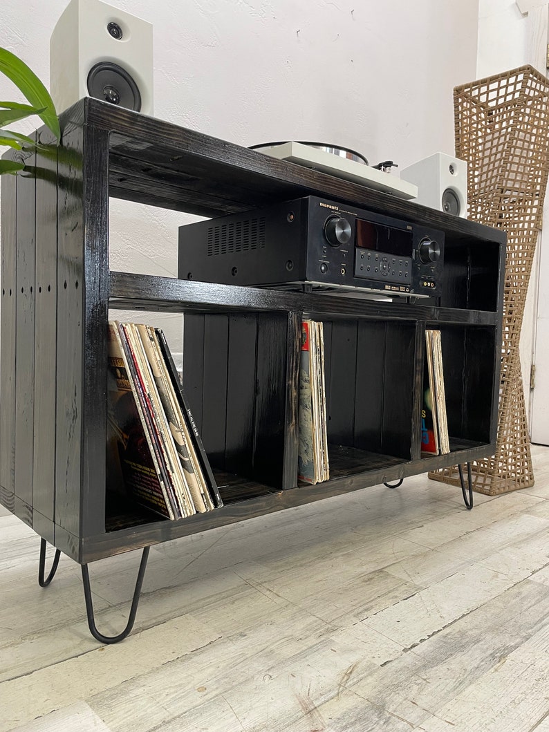 May include: Black wooden record player stand with four shelves, a turntable, and an amplifier. The stand has hairpin legs and is filled with vinyl records.