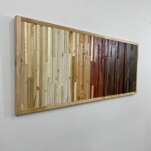 May include: A rectangular wall art piece made of reclaimed wood. The wood is arranged in a gradient pattern, starting with light wood on the left and transitioning to darker wood on the right. The wood is framed in a natural wood frame.