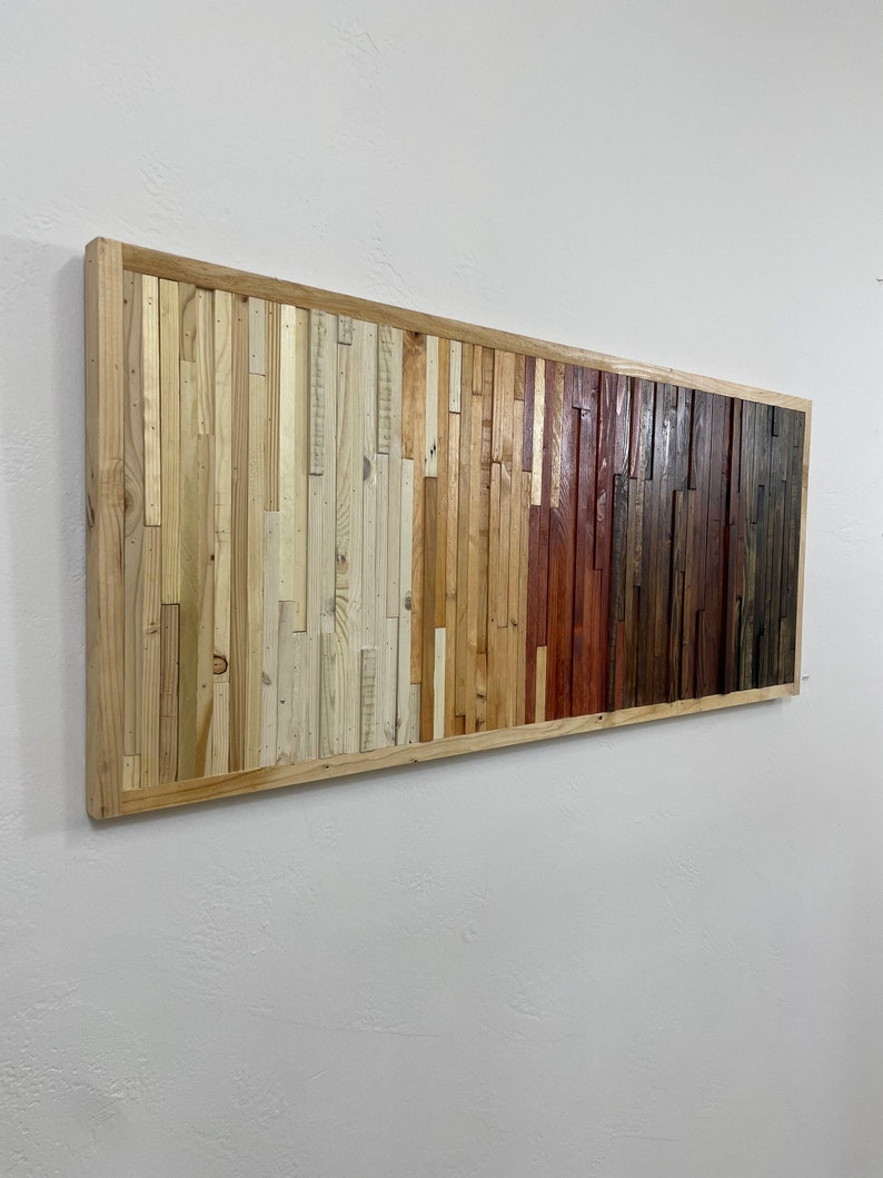 May include: A rectangular wall art piece made of reclaimed wood. The wood is arranged in a gradient pattern, starting with light wood on the left and transitioning to darker wood on the right. The wood is framed in a natural wood frame.