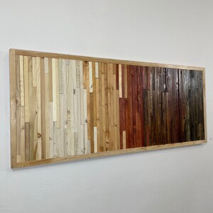 May include: A rectangular wall art piece made of wood planks in various shades of brown, beige, and white. The planks are arranged in a horizontal pattern, creating a gradient effect from light to dark.