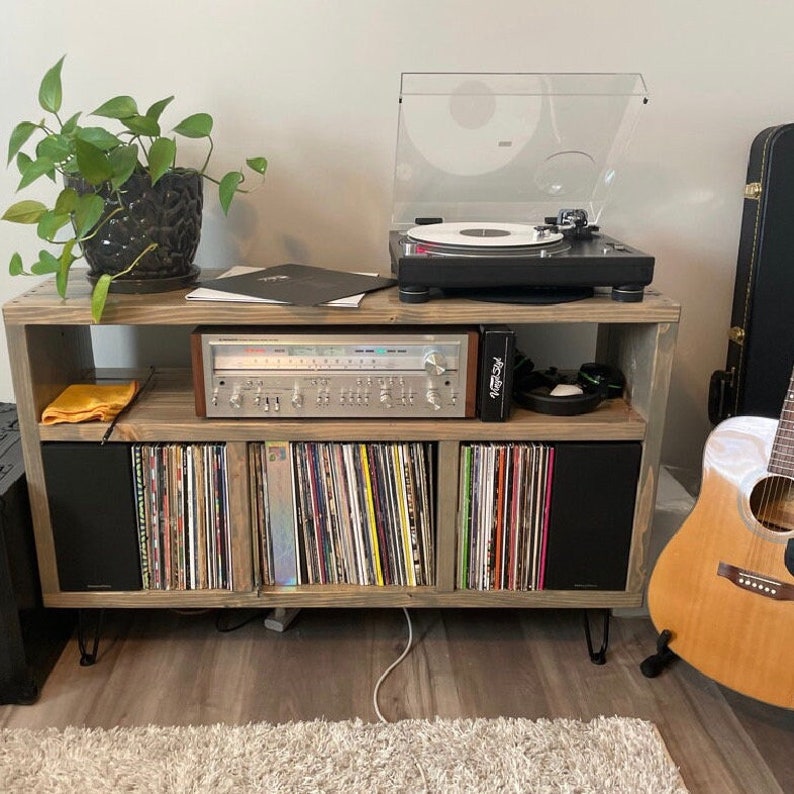 May include: A wooden record player stand with a turntable, receiver, and vinyl records. The stand has a rustic brown finish and black speakers. A yellow cloth is on the top shelf.