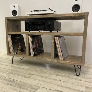May include: A rustic wooden record player stand with three shelves, black metal hairpin legs, and a turntable on the top shelf. The stand is holding a stereo receiver, a turntable, and vinyl records.