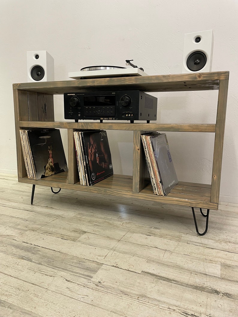 May include: A rustic wooden record player stand with three shelves, black metal hairpin legs, and a turntable on the top shelf. The stand is holding a stereo receiver, a turntable, and vinyl records.