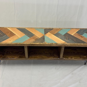 May include: A wooden bench with three storage compartments and a herringbone pattern top in shades of brown, blue, and green. The bench has black hairpin legs.