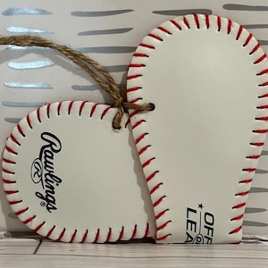 May include: White heart-shaped ornament with red stitching, featuring the Rawlings logo and "Official League" text. The ornament has a twine string for hanging.