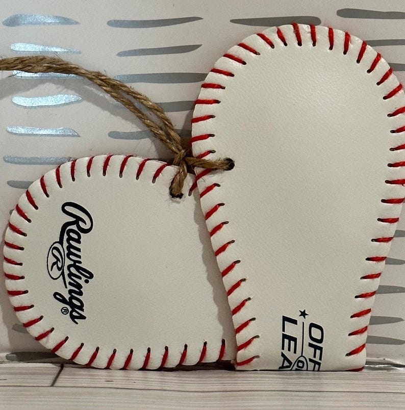 May include: White heart-shaped ornament with red stitching, featuring the Rawlings logo and "Official League" text. The ornament has a twine string for hanging.
