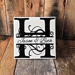May include: A white square tile with a black letter H with decorative flourishes. The name "Jason & Beth" is written in a black cursive font on a black horizontal line.