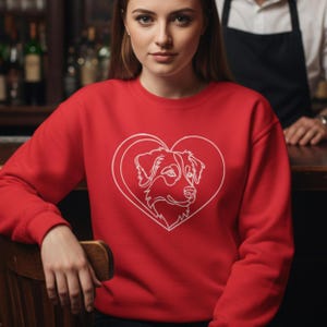Peut inclure: Un sweat-shirt rouge avec un dessin blanc d'une tête de chien dans un cœur. Le sweat-shirt à col rond est fait d'une matière douce. Le dessin du chien est centré sur le devant du vêtement.