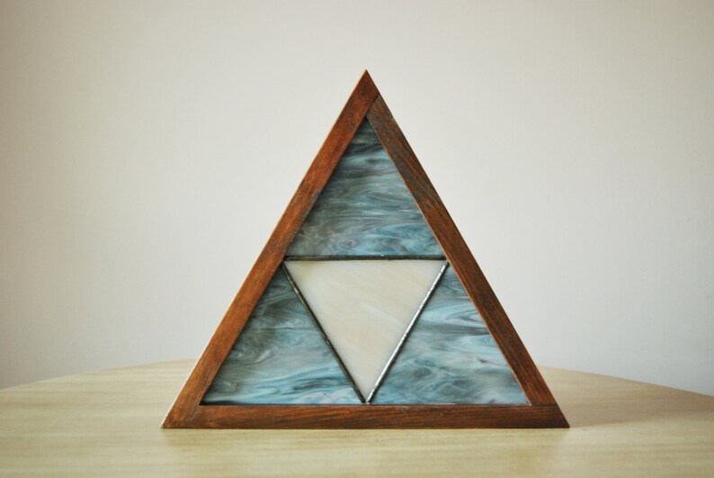 K&ouml;nnte beinhalten: Ein dreieckiger Holzrahmen mit einem Glasmosaik-Design. Das Glas ist blau und wei&szlig;, mit einem wei&szlig;en Dreieck in der Mitte.