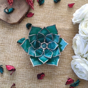 May include: A teal green stained glass succulent with a silver outline. The succulent is shaped like a flower with multiple layers of petals.