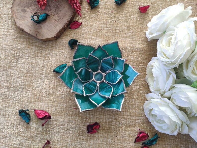 May include: A teal green stained glass succulent with a silver outline. The succulent is shaped like a flower with multiple layers of petals.