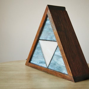 K&ouml;nnte beinhalten: Eine dreieckige Holzlampe mit einem Buntglasdesign, das ein wei&szlig;es Dreieck innerhalb von zwei blauen Dreiecken zeigt.