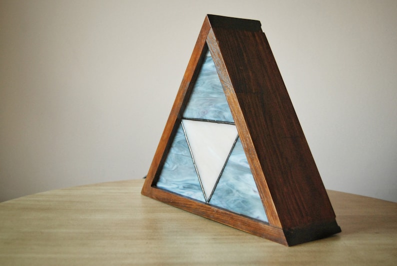 K&ouml;nnte beinhalten: Eine dreieckige Holzlampe mit einem Buntglasdesign, das ein wei&szlig;es Dreieck innerhalb von zwei blauen Dreiecken zeigt.