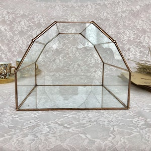 May include: A clear glass geometric box with a copper frame. The box is empty and has a reflective surface.