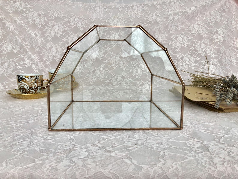 May include: A clear glass geometric box with a copper frame. The box is empty and has a reflective surface.