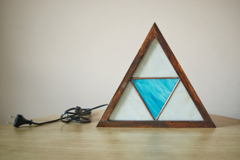 K&ouml;nnte beinhalten: Eine dreieckige Holzlampe mit einem Buntglasdesign. Das Glas ist wei&szlig; mit einem blauen Dreieck in der Mitte.