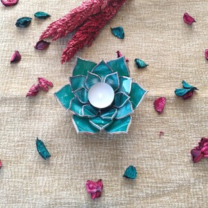 May include: Teal glass candle holder shaped like a succulent plant with a white tea light candle inside.
