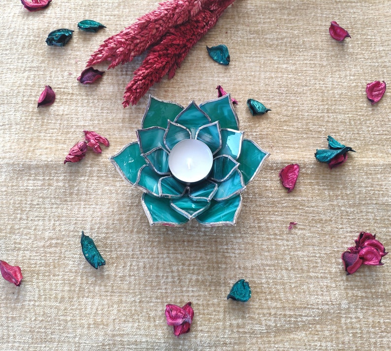 May include: Teal glass candle holder shaped like a succulent plant with a white tea light candle inside.