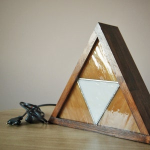 K&ouml;nnte beinhalten: Eine dreieckige Holzlampe mit einem Buntglasdesign, das ein wei&szlig;es Dreieck innerhalb von zwei gelben Dreiecken zeigt.