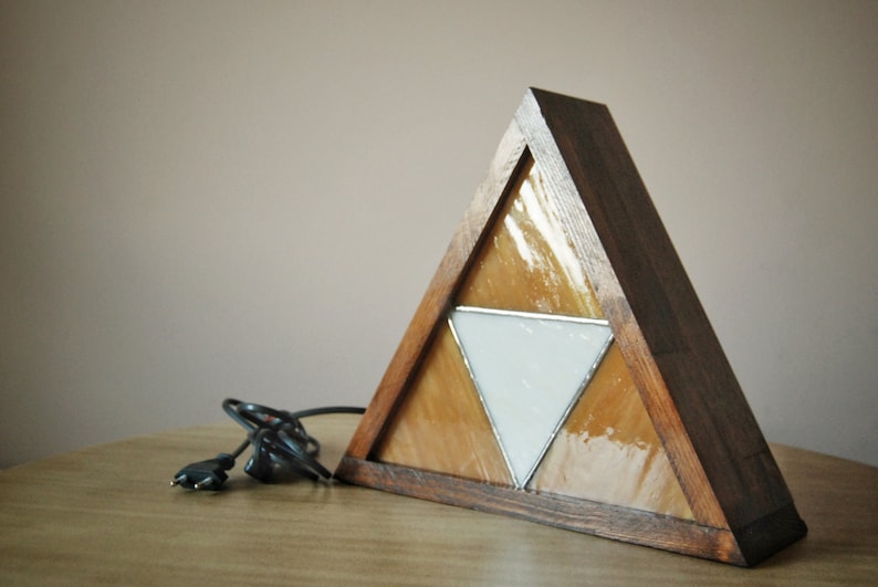 K&ouml;nnte beinhalten: Eine dreieckige Holzlampe mit einem Buntglasdesign, das ein wei&szlig;es Dreieck innerhalb von zwei gelben Dreiecken zeigt.