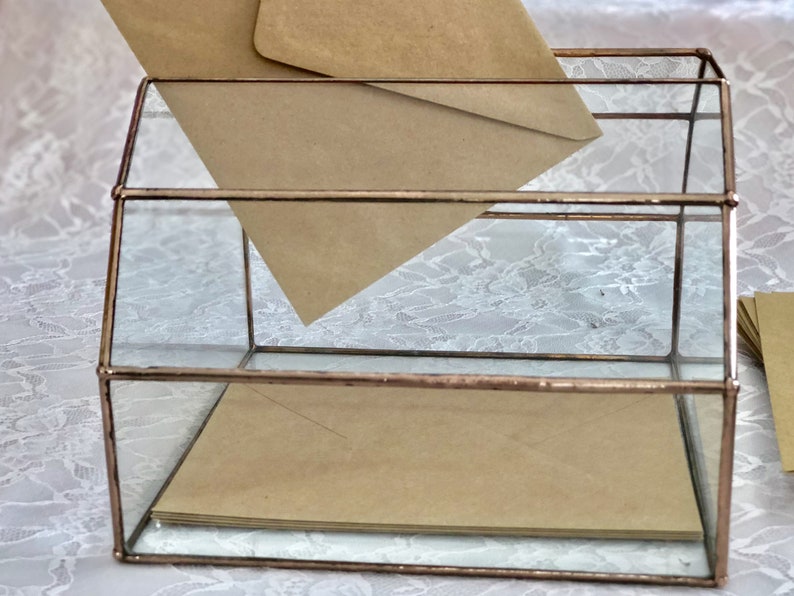 May include: A glass box with a copper frame, used for holding envelopes. The box has two levels and is filled with brown envelopes.