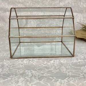 May include: A clear glass display case with a gold metal frame. The case has three shelves and a peaked roof.