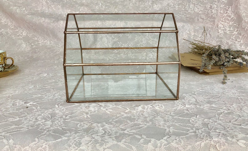 May include: A clear glass display case with a gold metal frame. The case has three shelves and a peaked roof.