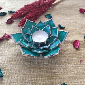 May include: Teal glass candle holder shaped like a flower with a silver trim. A white tea light candle is inside the holder.