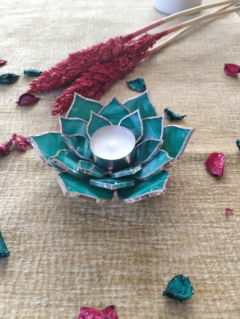 May include: Teal glass candle holder shaped like a flower with a silver trim. A white tea light candle is inside the holder.