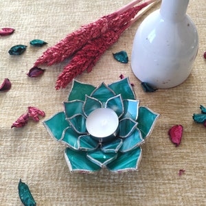 May include: Teal glass candle holder shaped like a succulent with a white tea light candle inside.