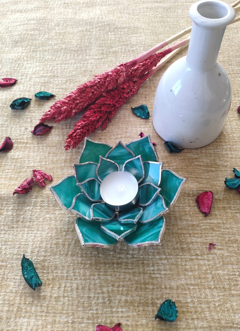 May include: Teal glass candle holder shaped like a succulent with a white tea light candle inside.