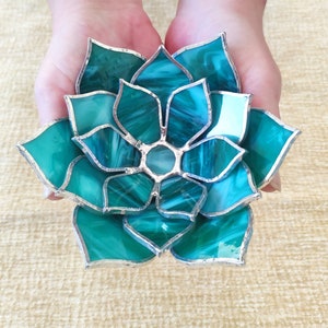 May include: A teal blue stained glass succulent with silver accents. The succulent is made of individual pieces of glass that are joined together with silver solder.