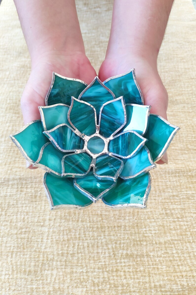 May include: A teal blue stained glass succulent with silver accents. The succulent is made of individual pieces of glass that are joined together with silver solder.