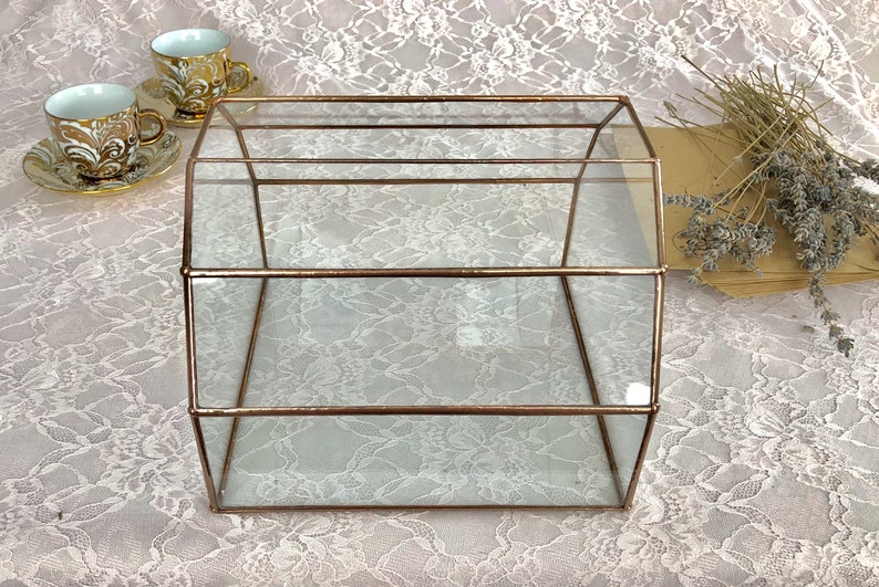 May include: A clear glass box with a copper frame. The box has three shelves and is sitting on a white lace tablecloth.