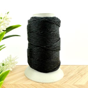 May include: A spool of black waxed cotton cord. The cord is wound tightly around the spool and is ready to be used for crafting or other projects.