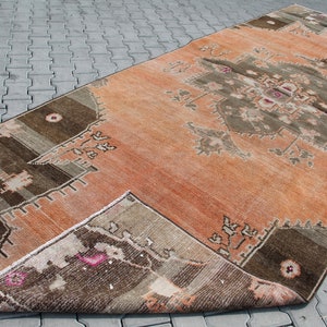 May include: An orange and brown vintage rug with a central geometric design. The rug has a distressed appearance, with faded colors and a worn texture. The rug is rectangular and appears to be made of woven material.