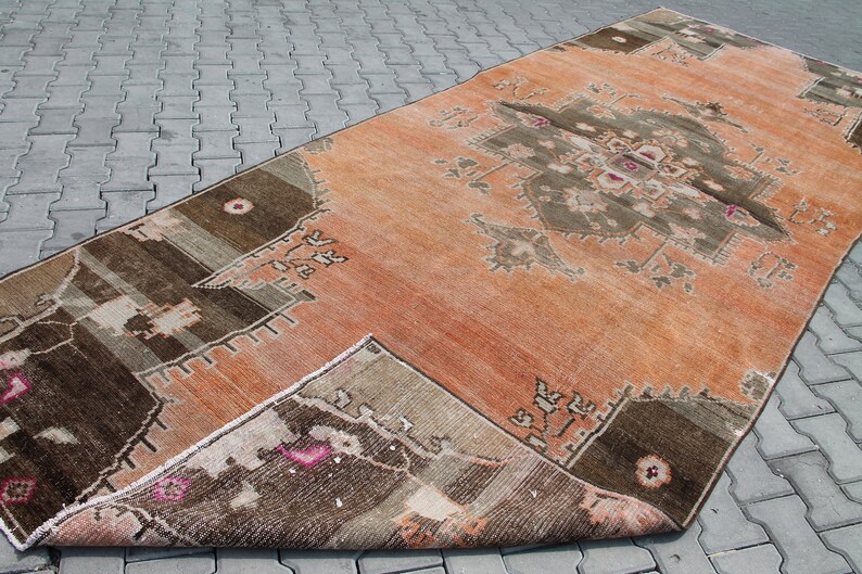 May include: An orange and brown vintage rug with a central geometric design. The rug has a distressed appearance, with faded colors and a worn texture. The rug is rectangular and appears to be made of woven material.