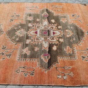 May include: An orange and brown patterned rug with a central geometric design. The rug features a symmetrical pattern with floral and geometric elements in shades of orange, brown, and cream. The rug is rectangular and appears to be made of woven material.