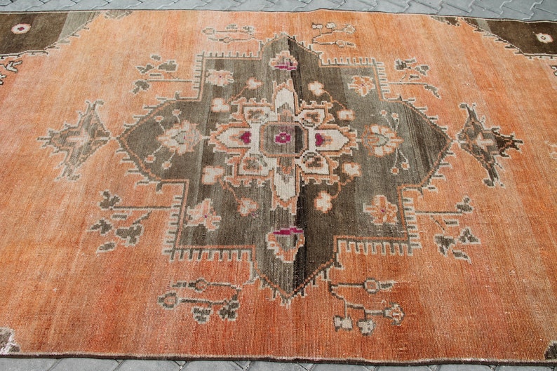 May include: An orange and brown patterned rug with a central geometric design. The rug features a symmetrical pattern with floral and geometric elements in shades of orange, brown, and cream. The rug is rectangular and appears to be made of woven material.