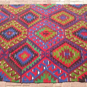 May include: A colorful rug with a geometric pattern in shades of red, green, blue, and black. The rug has a traditional design with intricate details.