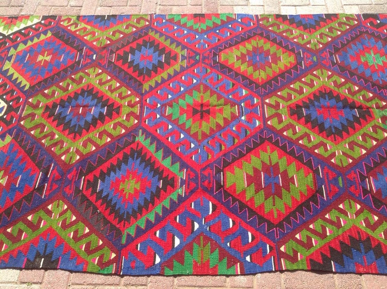 May include: A colorful rug with a geometric pattern in shades of red, green, blue, and black. The rug has a traditional design with intricate details.
